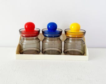 Juego de tarros de escritorio vintage con tapas de bolas de plástico de colores primarios y soporte para clips y gomas elásticas.