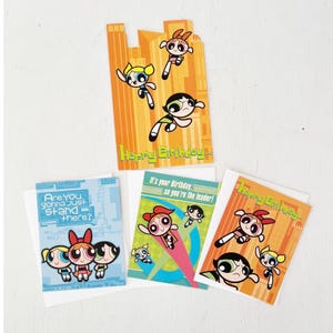 May include: Four Powerpuff Girls themed greeting cards. One card has a cityscape design with the words "Happy Birthday." Another card says "Are You Gonna Just Stand There?" The other two cards say "It's your Birthday, So you're the leader!" and "Happy Birthday."