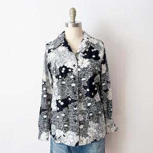 Può includere: Camicia a maniche lunghe con motivo floreale in bianco e nero. La camicia è esposta su un manichino, mettendo in risalto il colletto e i polsini. Il design floreale presenta grandi fiori stilizzati.