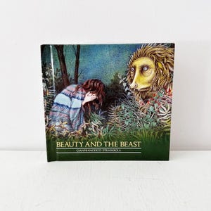 May include: A hardcover book titled "Beauty and the Beast" with an illustration of a woman in a forest, covering her face, and a beast with yellow fur. The book's title and author's name are printed in white.