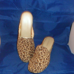 May include: A pair of leopard print slippers with a brown and gold color scheme. The slippers are made of a soft, fuzzy material and have a comfortable fit.