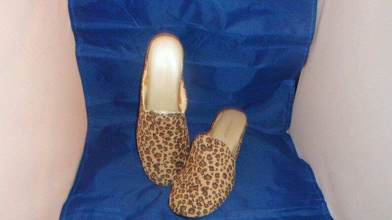 May include: A pair of leopard print slippers with a brown and gold color scheme. The slippers are made of a soft, fuzzy material and have a comfortable fit.