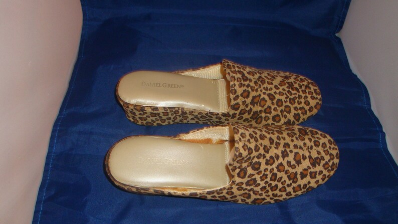 May include: A pair of leopard print house slippers with a wedge heel. The slippers are made by the brand "Camille Green".