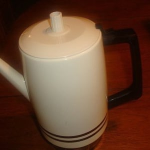 May include: A white electric coffee pot with a black handle and a black stripe around the bottom.