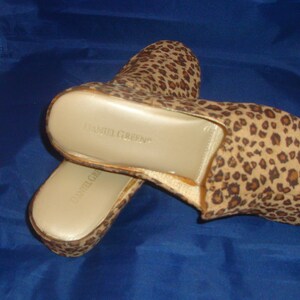 May include: A pair of brown and tan leopard print slippers with a gold insole. The slippers have the text "Daniel Green" printed on the insole.