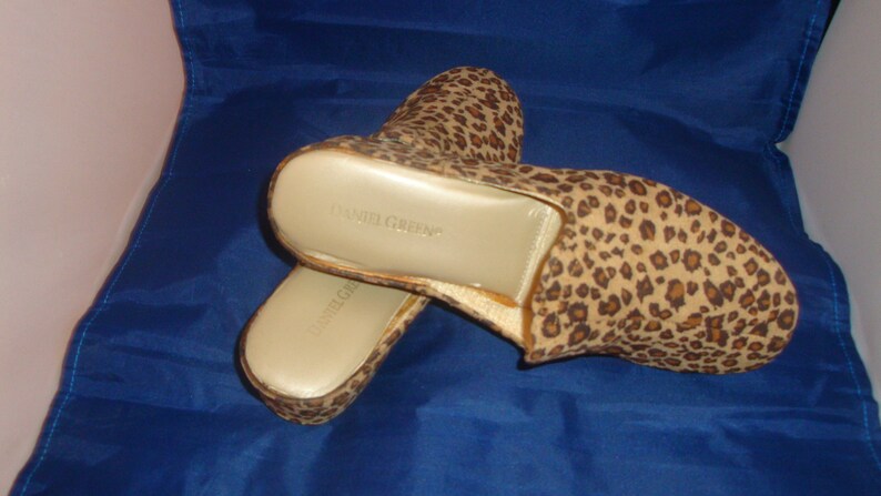 May include: A pair of brown and tan leopard print slippers with a gold insole. The slippers have the text "Daniel Green" printed on the insole.