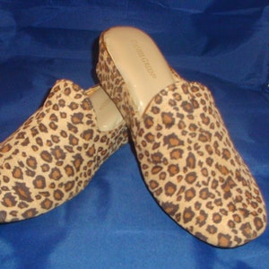 May include: A pair of leopard print slip-on shoes with a low heel. The shoes are made of a soft, suede-like material and have a comfortable fit.