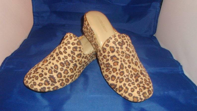 May include: A pair of leopard print slip-on shoes with a low heel. The shoes are made of a soft, suede-like material and have a comfortable fit.