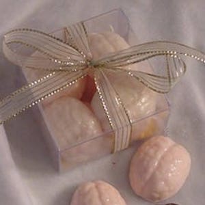 May include: A clear plastic box filled with pink and brown brain-shaped chocolates, tied with a gold ribbon.  The box is sitting on a white surface, and there are three additional chocolates outside the box.