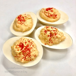 May include: Four white chocolate deviled eggs topped with a creamy filling and red sprinkles.  ChocolateFantasies.com IslandGirlGourmet on Etsy