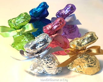 May include: Six foil-wrapped chocolate bunnies in various colors, including green, blue, purple, pink, silver, and gold. Each bunny has a ribbon tied around its neck.