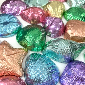 May include: Assortment of foil-wrapped chocolate candies in various colors, including green, blue, purple, pink, and gold. The candies are shaped like seashells and stars.
