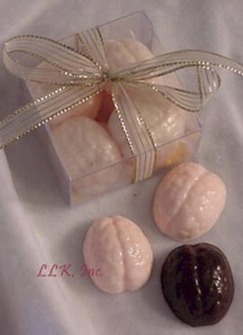 May include: A clear plastic box filled with pink and brown brain-shaped chocolates, tied with a gold ribbon.  The box is sitting on a white surface, and there are three additional chocolates outside the box.