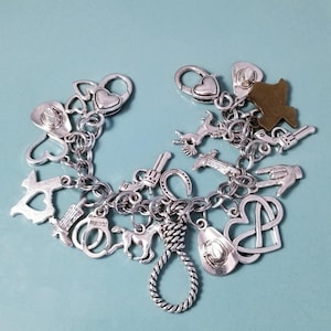 May include: Silver charm bracelet with cowboy-themed charms. The bracelet features charms shaped like cowboy hats, horses, revolvers, hearts, and a rope noose. The bracelet is on a light blue background.