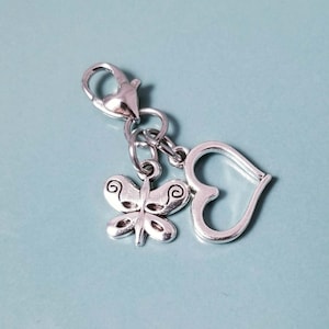 May include: A silver-toned metal charm featuring a lobster claw clasp attached to two dangling pendants. One pendant is a butterfly with etched swirl details on its wings, and the other pendant is a simple, open-frame heart shape.