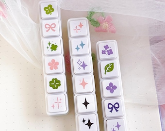 May include: Three white rectangular mechanical keyboard macro pads, each featuring six square keys with printed icons including green clovers, pink bows, blue and purple stars, pink cherry blossoms, and purple flowers.