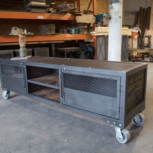 May include: A gray metal industrial style media console with two doors, two shelves, and four wheels. The doors have a wire mesh insert and the console has a distressed finish.