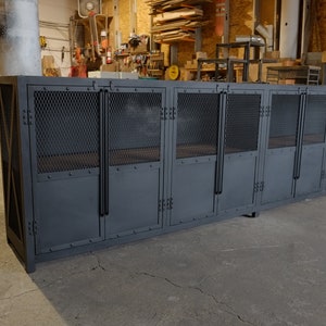 May include: A large, industrial-style cabinet with multiple compartments. The cabinet is painted a dark gray and features metal mesh panels on the upper doors and solid doors below. The cabinet is designed for storage and has a sturdy, utilitarian appearance.