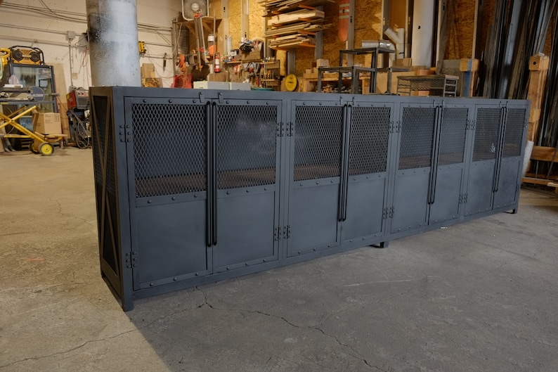 May include: A large, industrial-style cabinet with multiple compartments. The cabinet is painted a dark gray and features metal mesh panels on the upper doors and solid doors below. The cabinet is designed for storage and has a sturdy, utilitarian appearance.