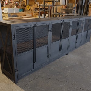 May include: A large, dark gray metal cabinet with multiple doors and mesh panels. The cabinet has a rectangular shape and is constructed with rivets and industrial-style handles. It is designed for storage.