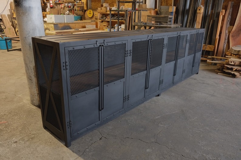 May include: A large, dark gray metal cabinet with multiple doors and mesh panels. The cabinet has a rectangular shape and is constructed with rivets and industrial-style handles. It is designed for storage.