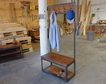 May include: A freestanding coat rack with a bench and shelf. The rack is made of metal and has a wooden top. The bench has a wooden seat and a metal frame. The shelf is made of wood and is located below the bench. A blue baseball cap hangs on the rack. A gray hoodie hangs on the rack. Two pairs of shoes are on the shelf.