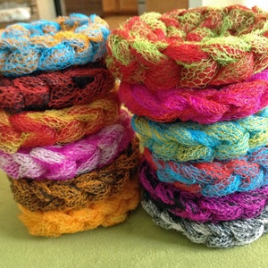 May include: A stack of colorful, crocheted scrubbers, made of a soft, mesh material. The scrubbers are in various colors, including red, pink, blue, green, and yellow.