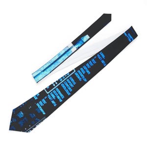 Puede incluir: Una corbata negra con un patrón azul similar a datos. La corbata está abierta, revelando un reverso blanco. El patrón incluye texto y formas rectangulares en tonos azules, creando un diseño de inspiración tecnológica. La corbata es de longitud estándar.