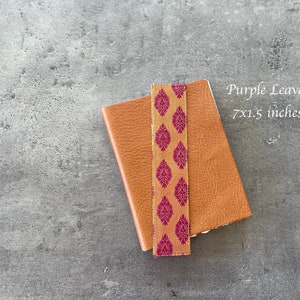 Może przedstawiać: Brązowy sk&oacute;rzany notes z zakładką w kolorze złotym i fioletowym. Notes ma wymiary 17,78 x 3,81 cm i zawiera napis "Purple Leaves" na okładce.