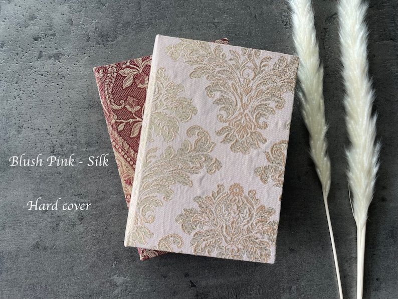 May include: Two hard cover journals with a blush pink silk cover and a gold and white damask pattern cover. The text "Blush Pink - Silk" and "Hard cover" is visible on the image.