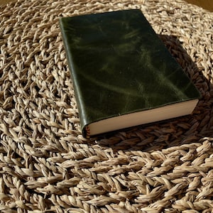 Op de afbeelding: Een donkergroen lederen gebonden dagboek of notitieboek op een geweven stro mat.