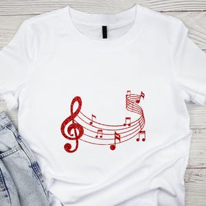 May include: White t-shirt with a red glitter design of a treble clef and musical notes.