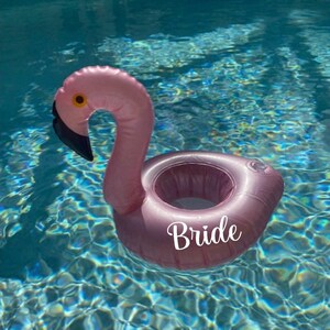 May include: Pink flamingo pool float with a cup holder and the word "Bride" printed on the side.