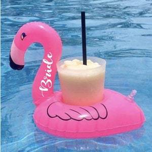 May include: Pink inflatable flamingo pool float with a clear cup holder and the word "Briola" written on the side. The float is in a blue swimming pool.