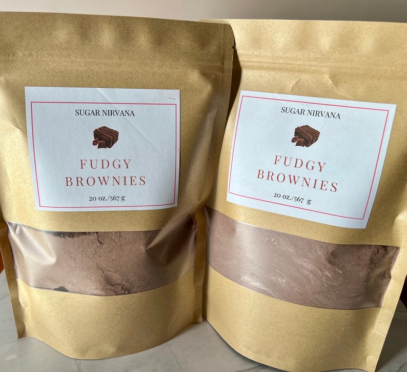 May include: Two brown paper bags with white labels that say "Sugar Nirvana" and "Fudgy Brownies" with a picture of a brownie. The bags contain a brown powder and the labels say "20 oz./567 g".