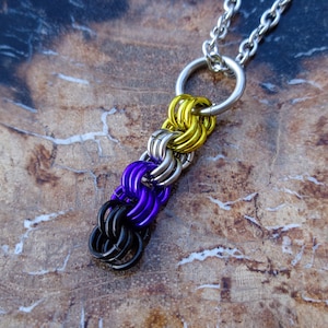 May include: A silver chain necklace with a pendant made of interconnected metal rings in black, purple, silver, and yellow colours.
