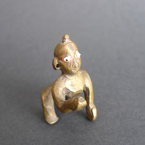 Könnte beinhalten: Eine kleine, goldfarbene Figur eines knienden Menschen mit rot und weiß bemalten Augen. Die Figur ist aus Messing und hat ein detailliertes Design.