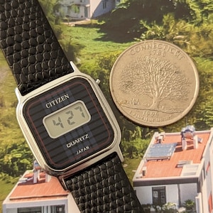 May include: A vintage Citizen digital watch with a black textured band and a silver-tone case. The watch face displays the time as 4:27. A Connecticut quarter coin is next to the watch.
