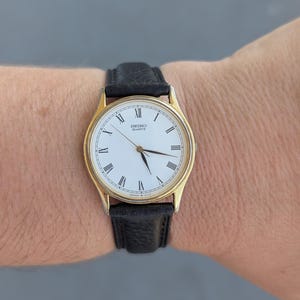 Vintage SEIKO Gold Tone Quartz Watch with White Face, New Black Leather Band and New Battery.  Best fits 8” wrist or smaller.
