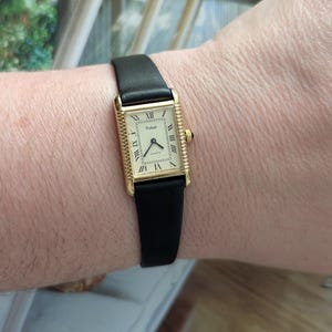 May include: A gold-coloured rectangular Pulsar quartz watch with a black leather strap. The watch face features Roman numerals and a small seconds dial. The watch is worn on a wrist.