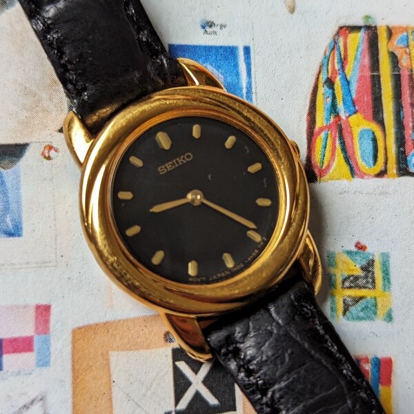 Vintage SEIKO Gold Tone Quartz Watch with Black Leather Band and New Battery. Best fits 6.5” wrist or smaller.