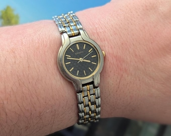 Vintage SEIKO Two Tone Quartz Watch with Round Bezel, Black Face and New Battery. Best fits 6.5” wrist or smaller.
