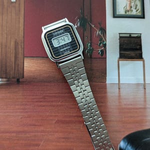 May include: A vintage Citizen Quartz watch with a silver-tone metal band. The watch face is black with a digital display showing the time 3:47. The watch has a rectangular shape with gold-tone accents and the brand name "CITIZEN" is visible.