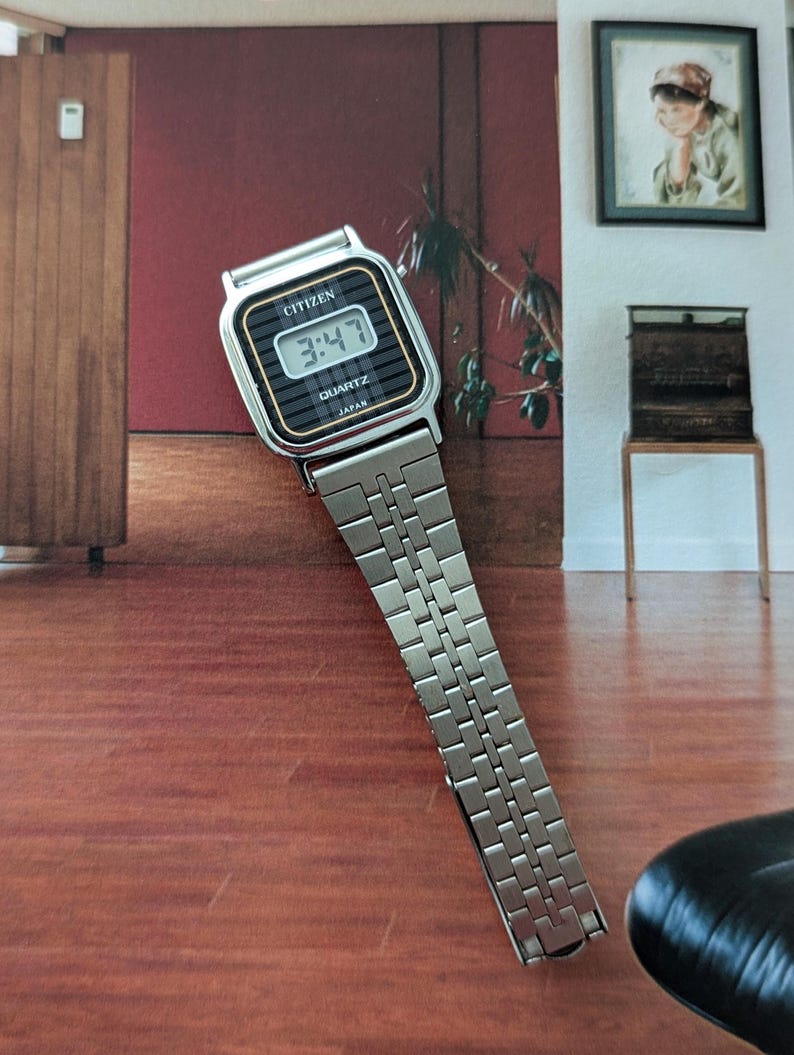 May include: A vintage Citizen Quartz watch with a silver-tone metal band. The watch face is black with a digital display showing the time 3:47. The watch has a rectangular shape with gold-tone accents and the brand name "CITIZEN" is visible.