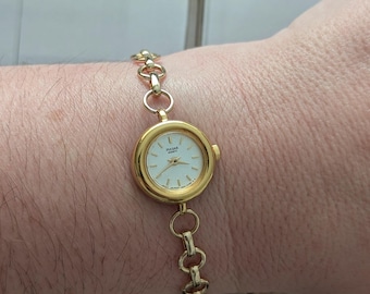 Vintage PULSAR Gold Tone Quartz Watch with Round Bezel, White Face, Matte Gold Band Detail and New Battery. Best fits 7” wrist or smaller.