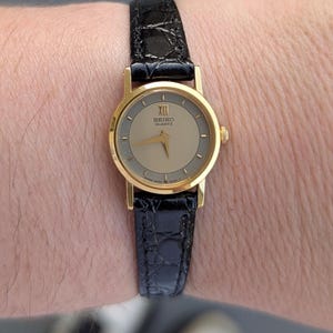 Vintage SEIKO Gold Tone Quartz Watch with Grey Detail, New Old Stock Black Leather Band and New Battery.  Best fits 6.5” wrist or smaller.