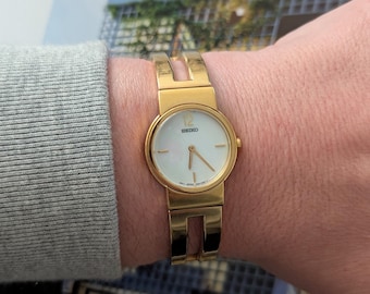 Vintage SEIKO Gold Tone Quartz Watch with Cream Tone Dial, Original Band and New Battery. This Best fits 7” wrist or smaller.