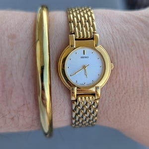 Vintage SEIKO Gold Tone Quartz Watch with White Starburst Face and New Battery. This Best fits 6” wrist or smaller.