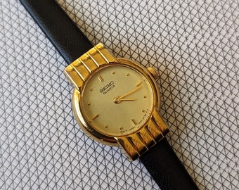 Montre à quartz vintage SEIKO avec lunette dorée, nouveau bracelet en cuir noir XL, batterie neuve et boîte d'origine. Convient parfaitement aux poignets jusqu'à 20 cm (8 po.).