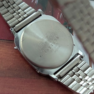 May include: A silver-toned Citizen watch with a rectangular face and a metal band. The watch back displays the Citizen brand name and model information. The band is a flexible, woven style.